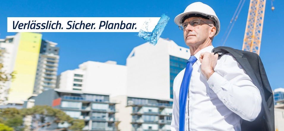 Ein Mann mit weißem Sicherheitshelm steht vor einem Gebäude