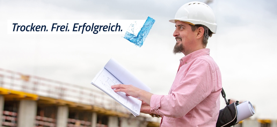Ein Mann mit weißem Helm steht auf einer Baustelle und hält eine Mappe in der Hand